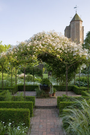 The White Garden in summer with Rosa mulliganii covering the pergola, and the Elizabethan Tower in the distance at Sissinghurst Castle Garden, near Cranbrook, Kent
